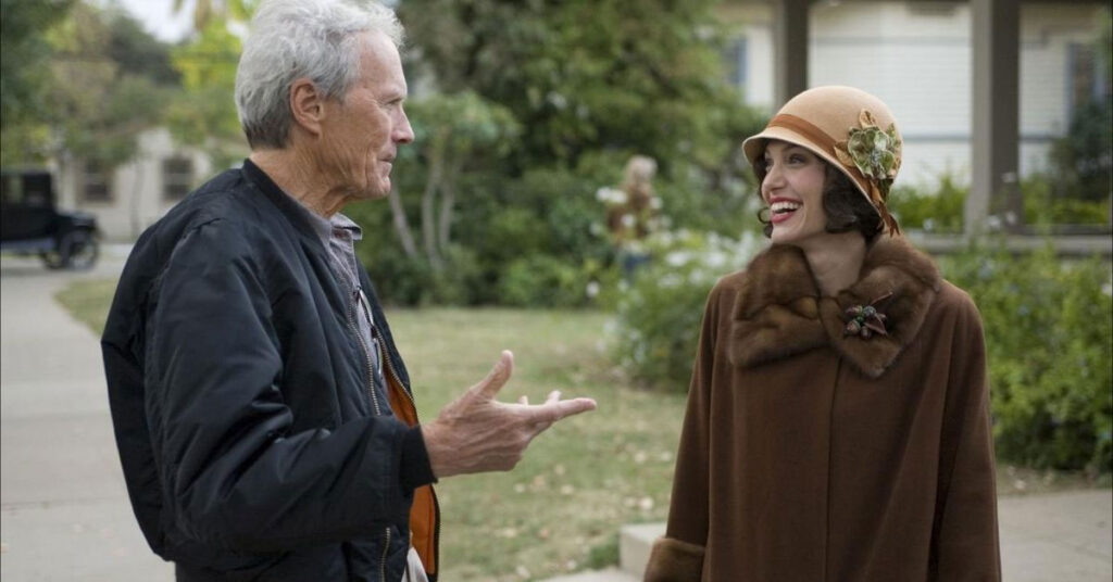 Obrazek pokazuje reżysera Clinta Eastwooda rozmawiającego z Angeliną Jolie na planie filmowym. Oboje się uśmiechają, scena ma charakter zza kulis, oddając lżejszy moment w przerwie od kręcenia poważnego filmu.
